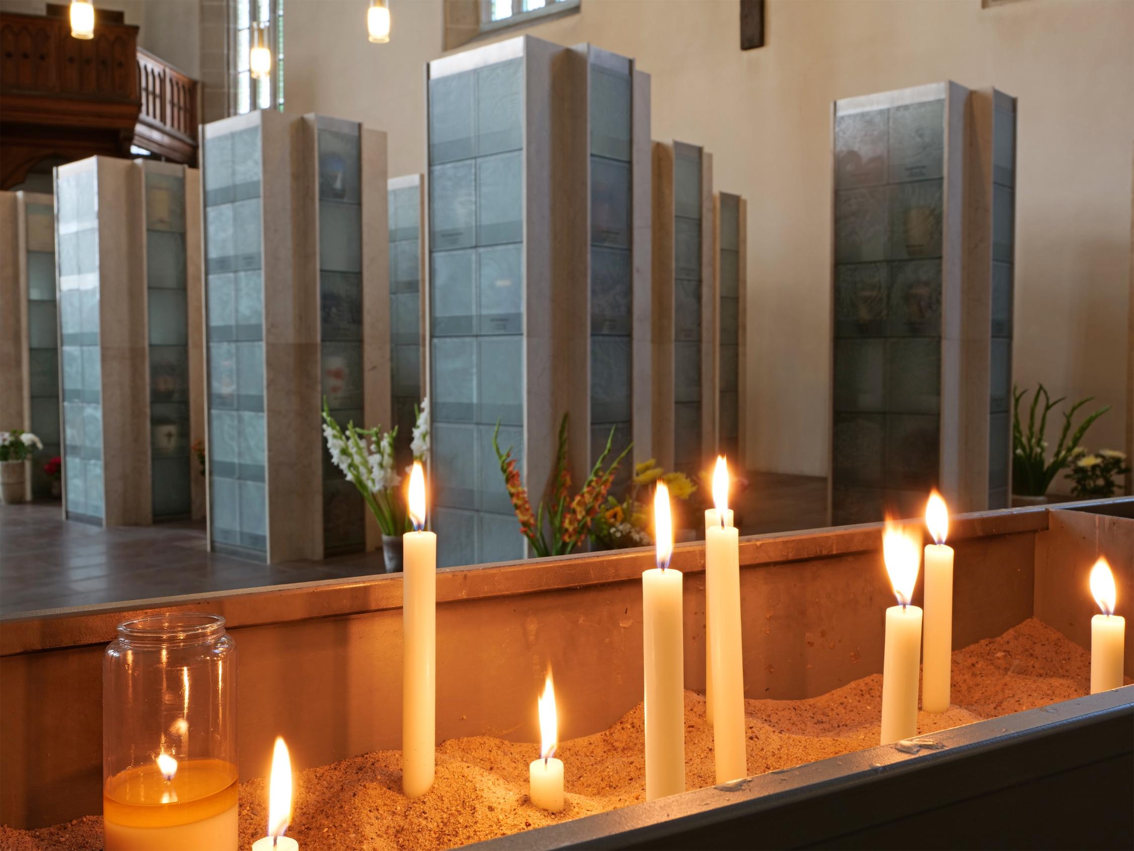 Brennende Kerzen im Sand vor modernen Grabnischen in einer Kirche